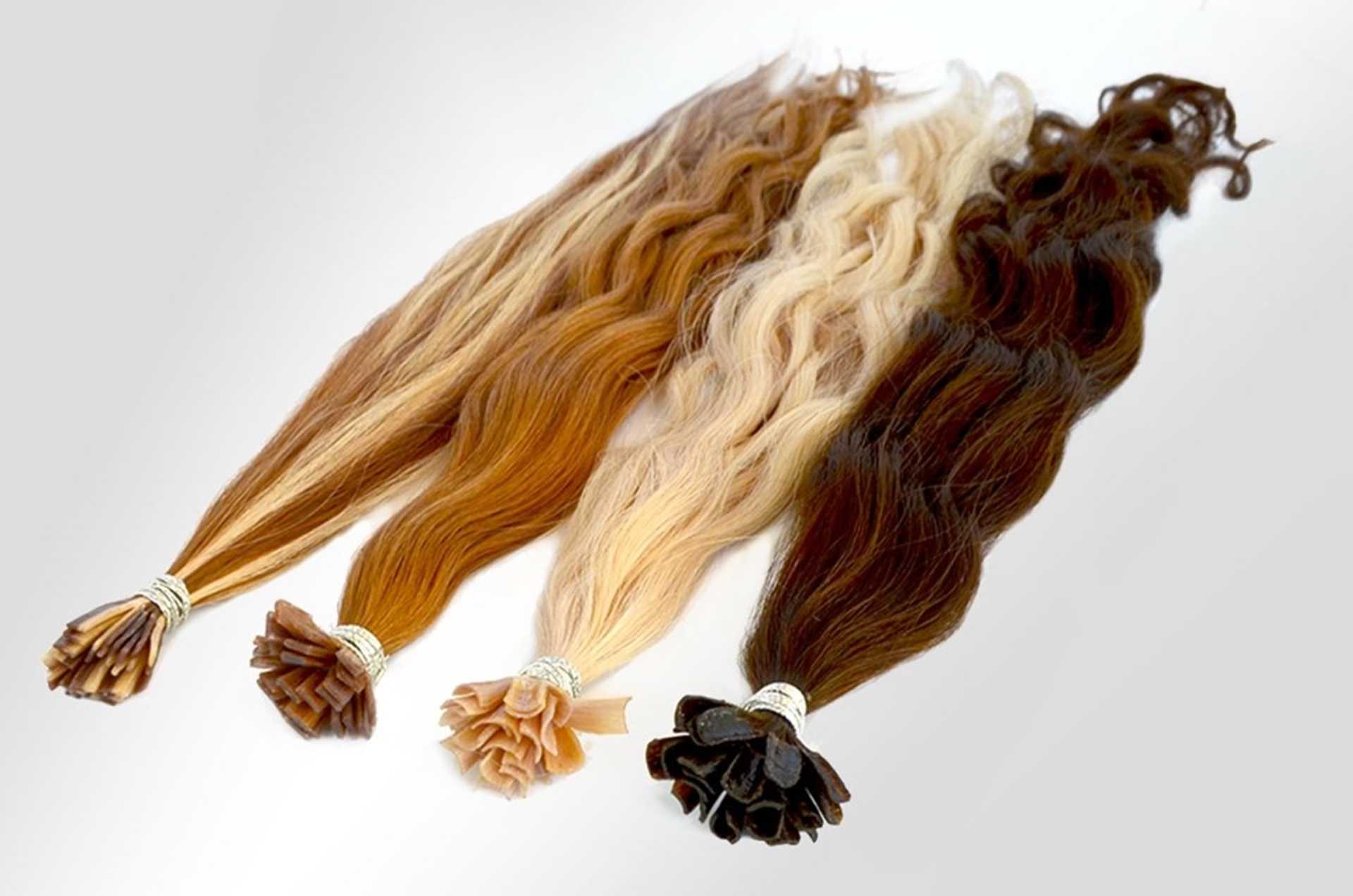 Four bundles of hair extensions in varying shades from dark brown to blonde, arranged on a table.