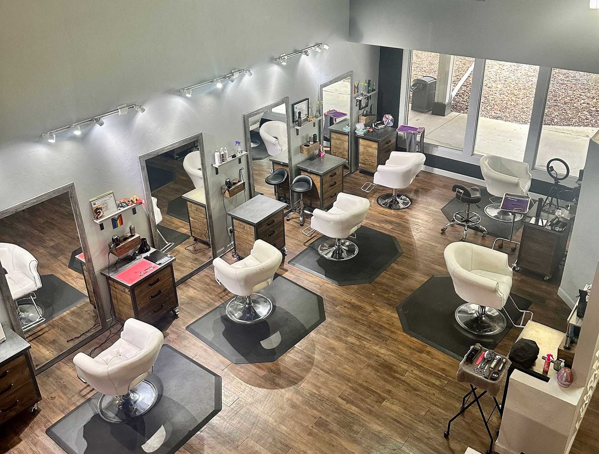 A modern, empty hair salon with white chairs, mirrors, and wooden flooring.