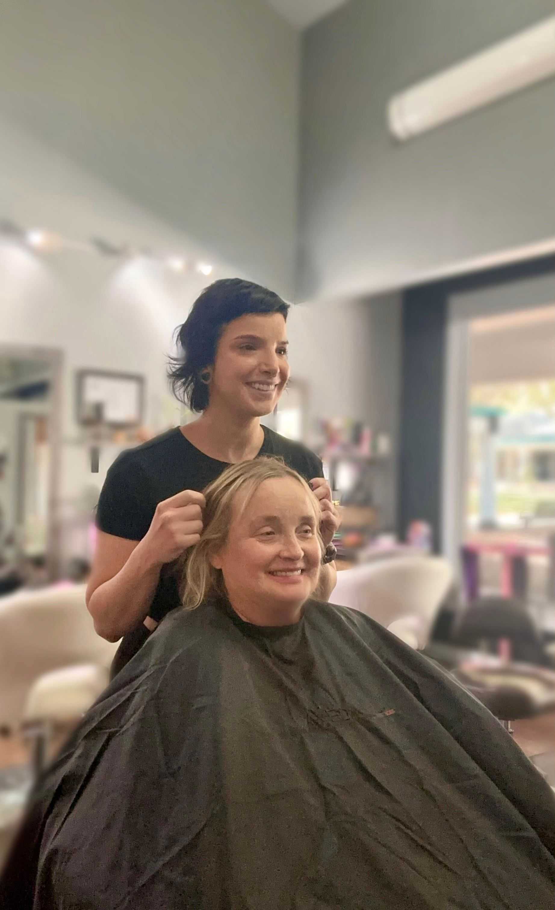 Smiling hairstylist working on a client's hair in a modern salon.