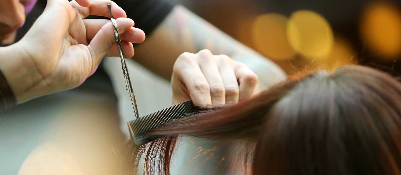 Hairdresser cutting client's hair with scissors and comb in a salon.